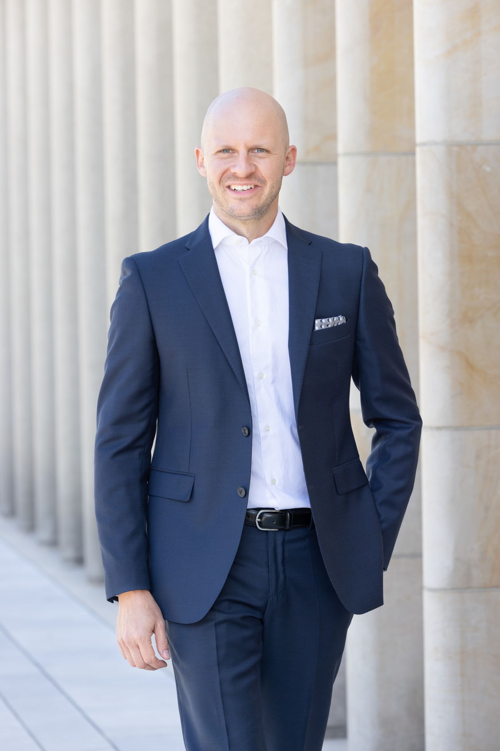 Christoph Dock in a navy suit, standing in front of stone columns